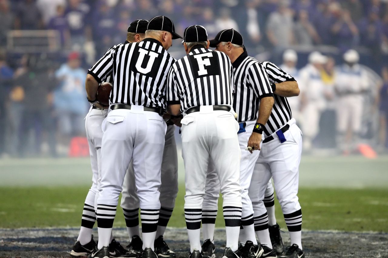 gallery-3 Group of sports officials in striped uniforms discussing on a football field.
