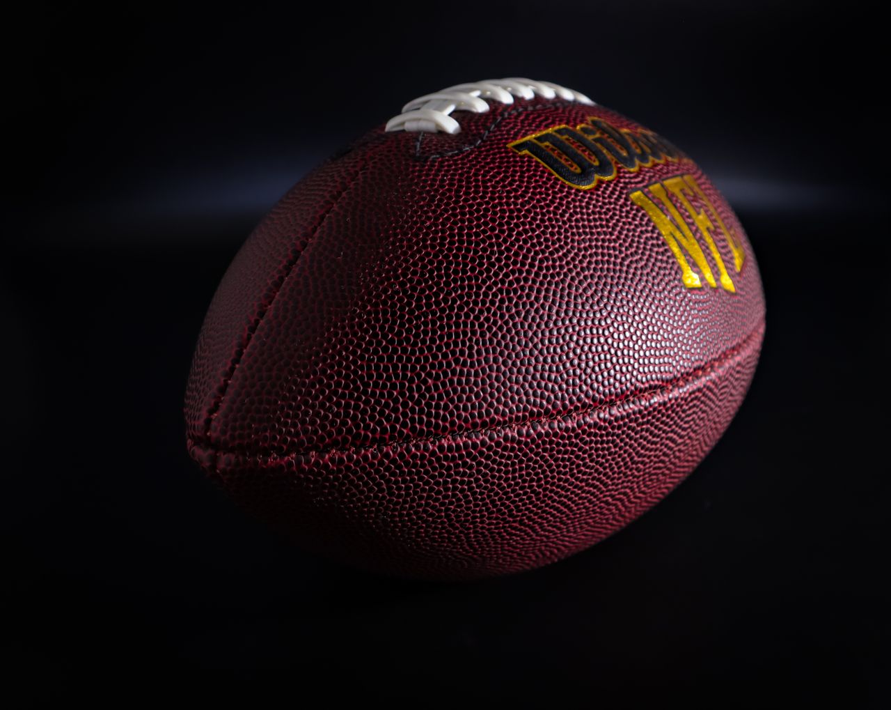 gallery-2 Detailed view of a traditional brown and white American football against a dark backdrop, highlighting texture.