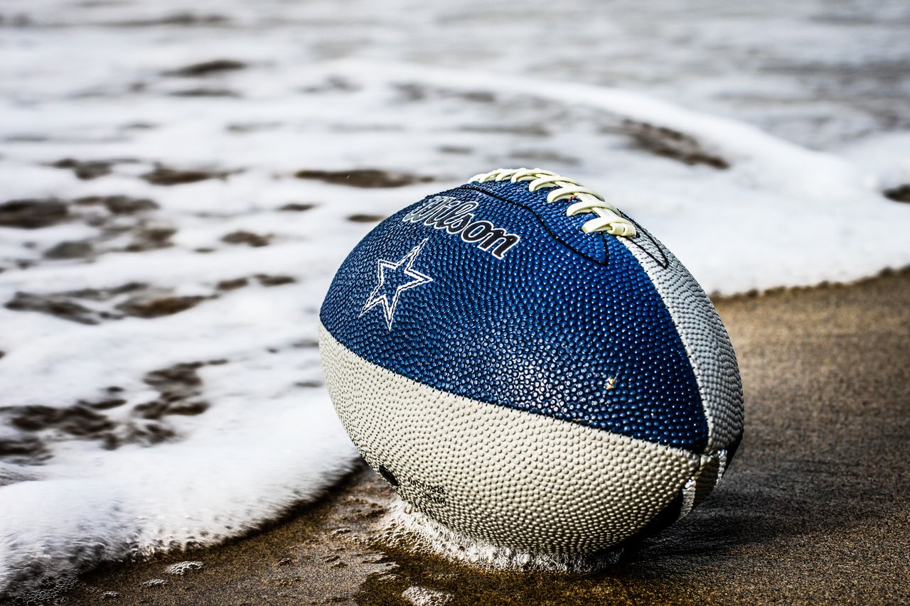 hero-img-01 Close-up of a blue football resting on wet sand by the ocean shore.
