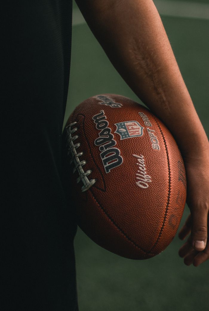 services-03 Detailed shot of a person's arm holding an official NFL football on a field.