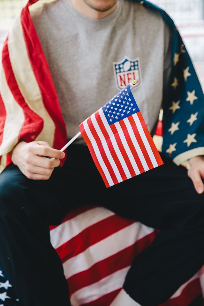 An adult holding a small American flag wrapped in a flag-themed outfit, celebrating patriotism.