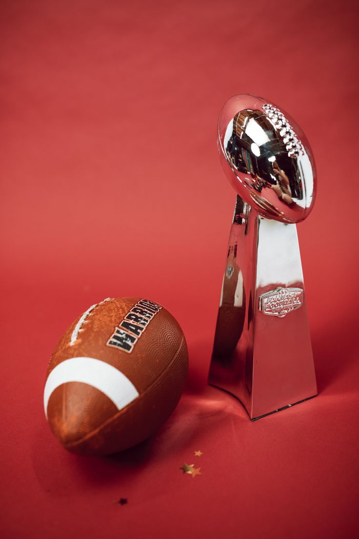 gallery-6 Football and silver trophy on red backdrop symbolizing victory and achievement.